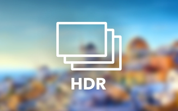 Белый логотип HDR (высокий динамический диапазон) с тремя перекрывающимися экранами на размытом, красочном ландшафтном фоне.