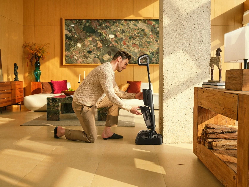 Чоловік стає на одне коліно та вставляє резервуар для води в пилосос.