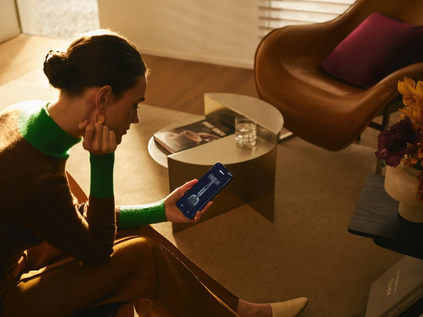 Жінка дистанційно керує пилососом за допомогою свого мобільного телефону.