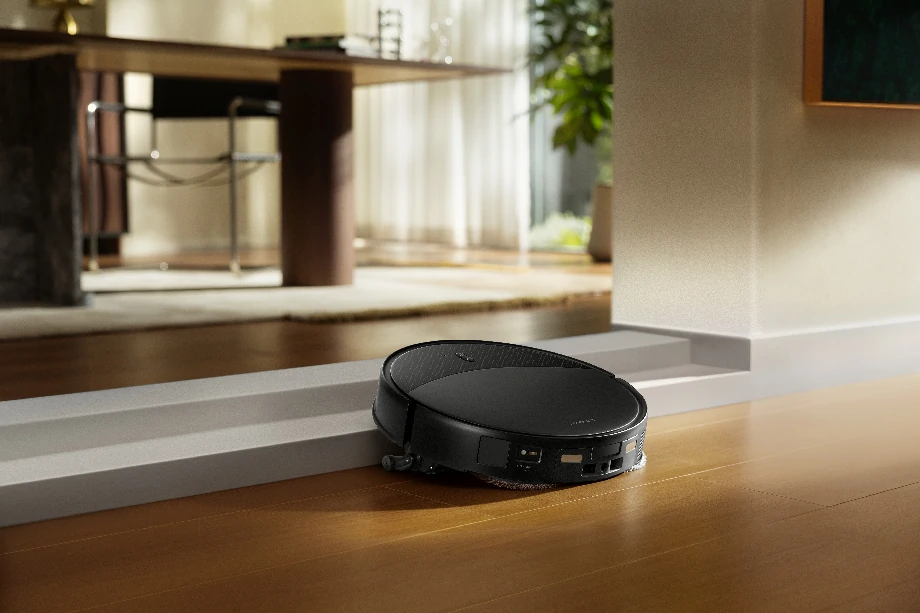 Чорний робот-прибиральник перетинає невеликий поріг, щоб потрапити до офісу.