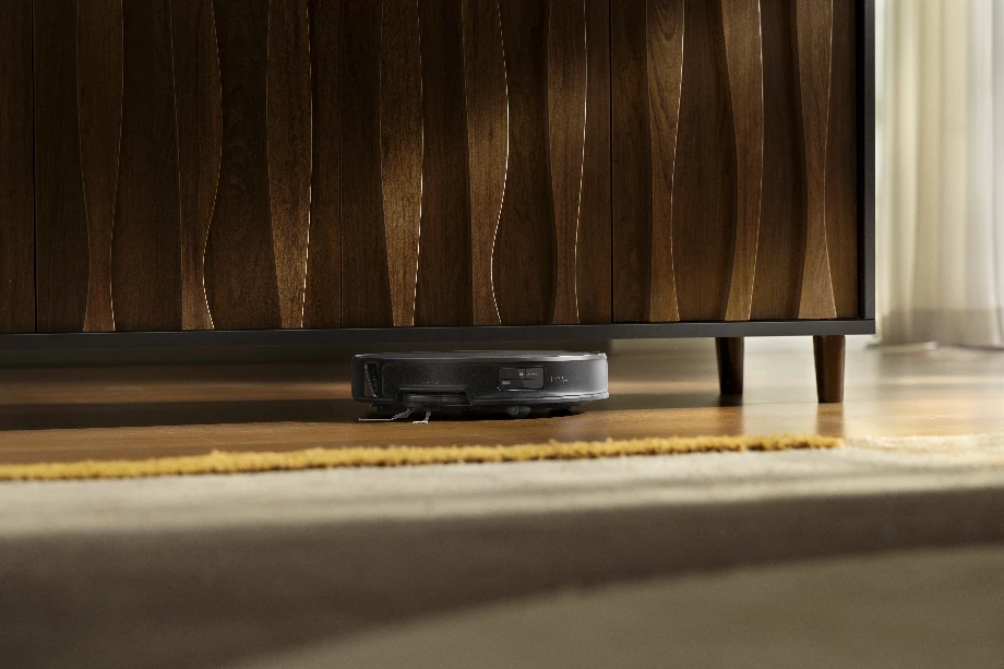 Чорний робот-прибиральник легко проникає у вузький простір між підлогою та нижньою частиною столу.