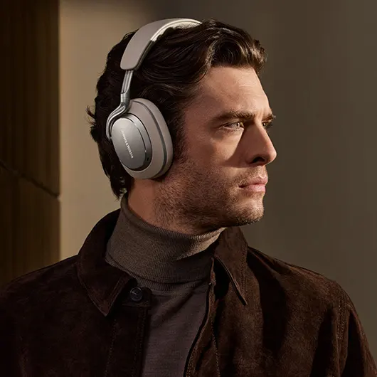 Чоловік дивиться праворуч і носить навушники Bowers & Wilkins Px8 S2 кольору «Теплий камінь».