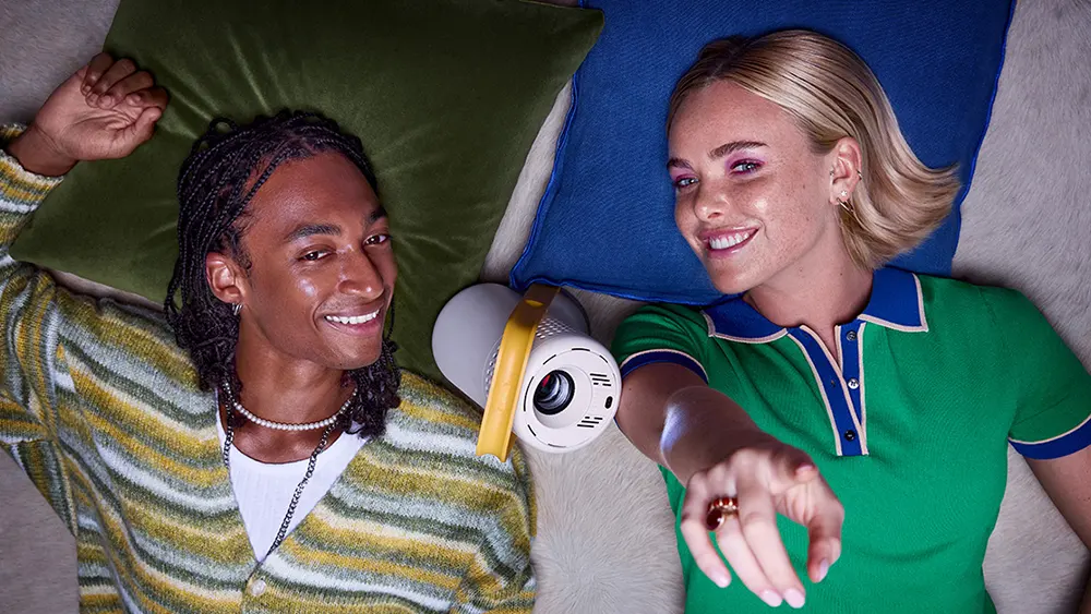 Усміхнені чоловік і жінка лежать на підлозі, між ними — XGIMI Vibe One, а жінка вказує пальцем на стелю.