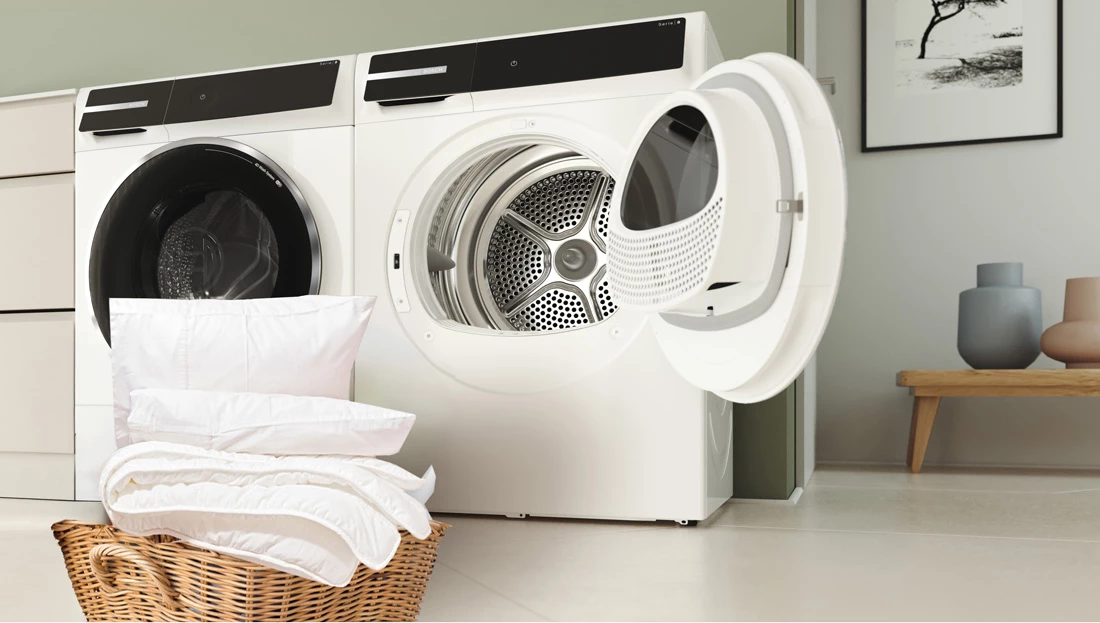 Сушарка стоїть біля стіни, а ліворуч — плетений кошик з білою білизною.