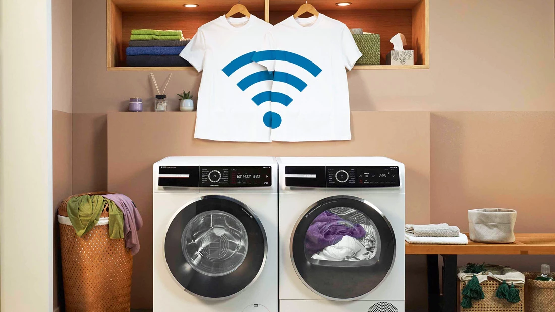 Сушарка та пральна машина розміщені поруч. На передньому плані рука тримає смартфон із застосунком Home Connect.