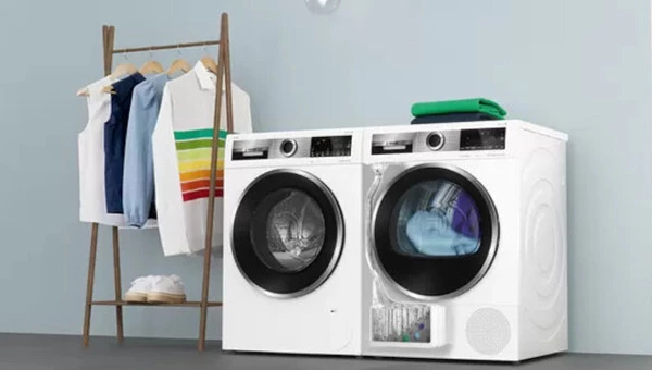 Пральна машина та сушарка Bosch стоять поруч, а поруч — вішалка для одягу.