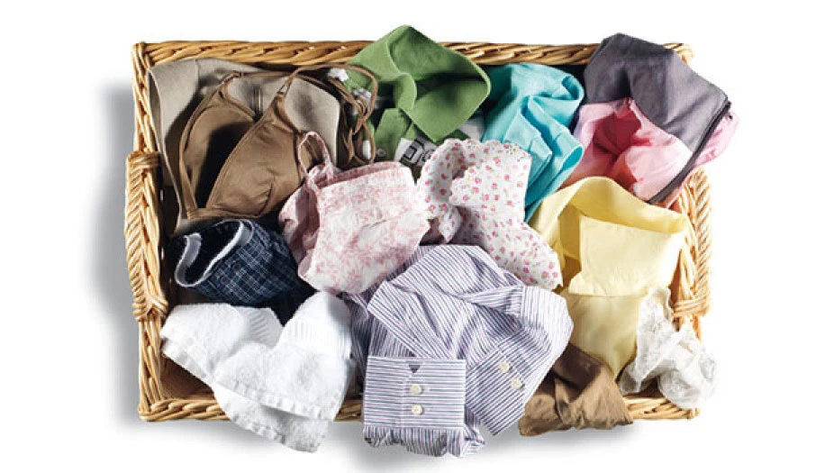 Плетений кошик, наповнений різнокольоровим одягом для прання або сушіння.