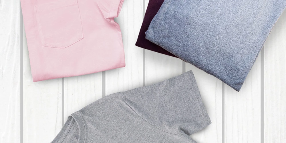 Складені футболки різних кольорів, розташовані на світлому дерев'яному фоні.