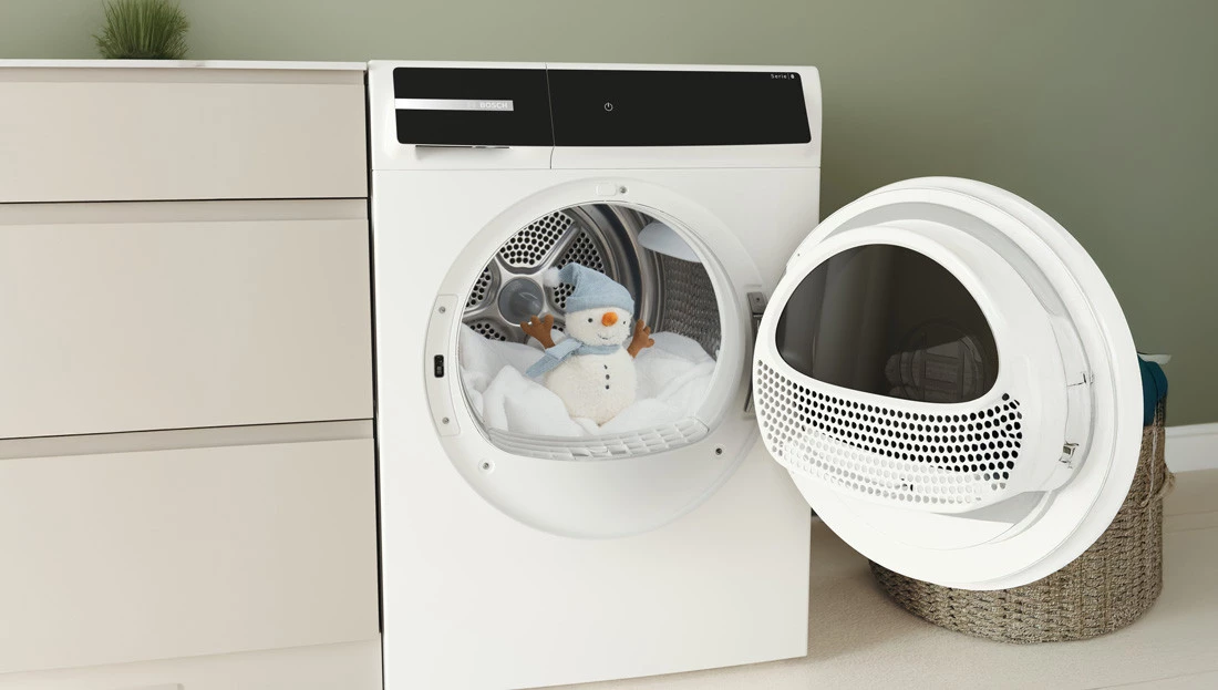 Біла сушарка Bosch з відчиненими дверцятами, плюшевий сніговик на рушниках у барабані.
