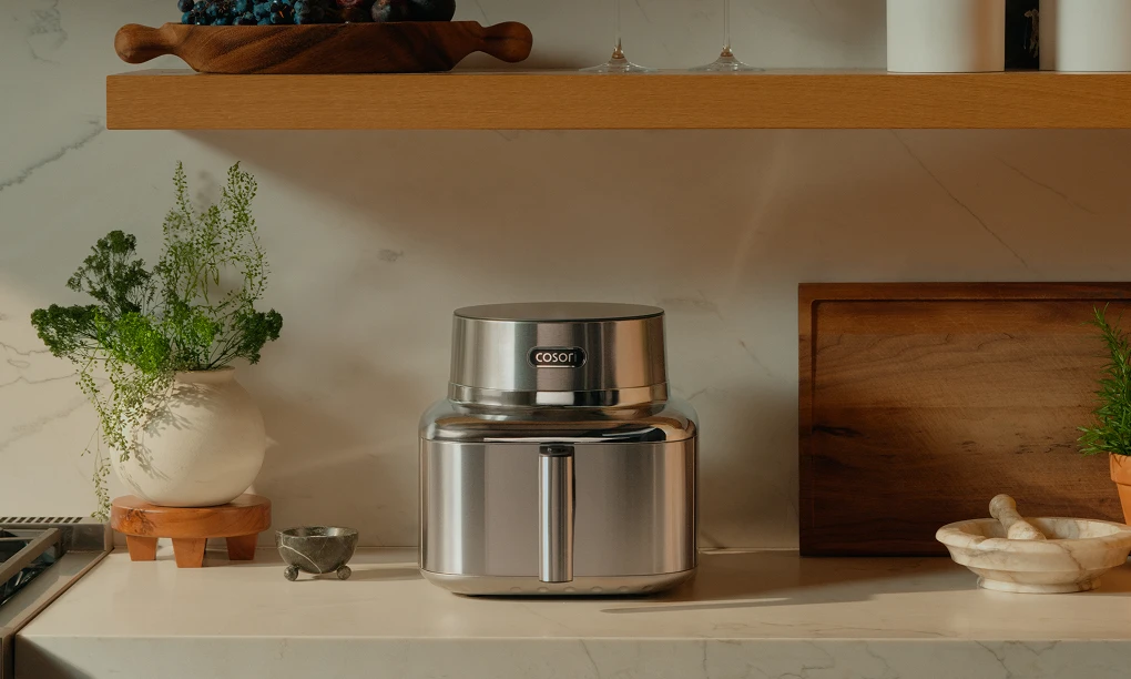 Срібна аерофритюрниця Cosori Iconic Single стоїть на світлій стільниці в сучасній, світлій кухні.