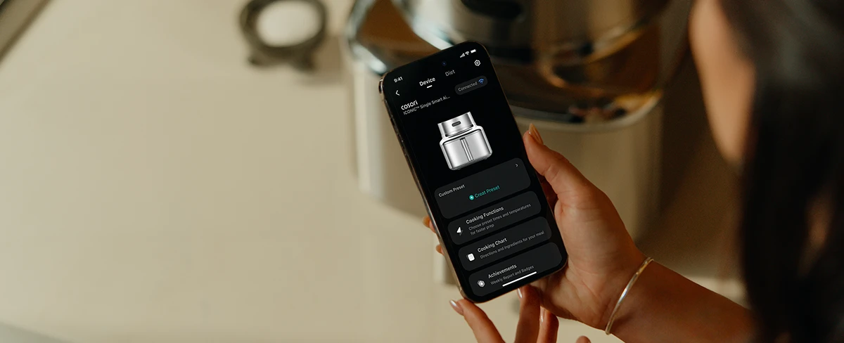 Смартфон з відкритим мобільним додатком Cosori для керування фритюрницею на тлі пристрою.