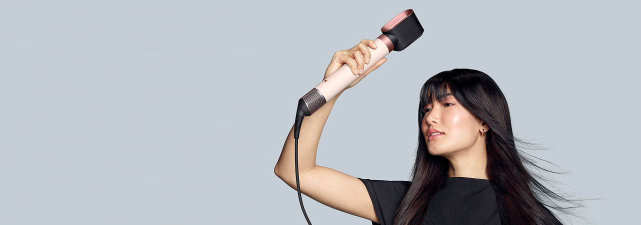 Модель з темним волоссям сушить волосся феном за допомогою мультистайлера Dyson Airwrap Coanda2x з насадкою для попереднього сушіння.