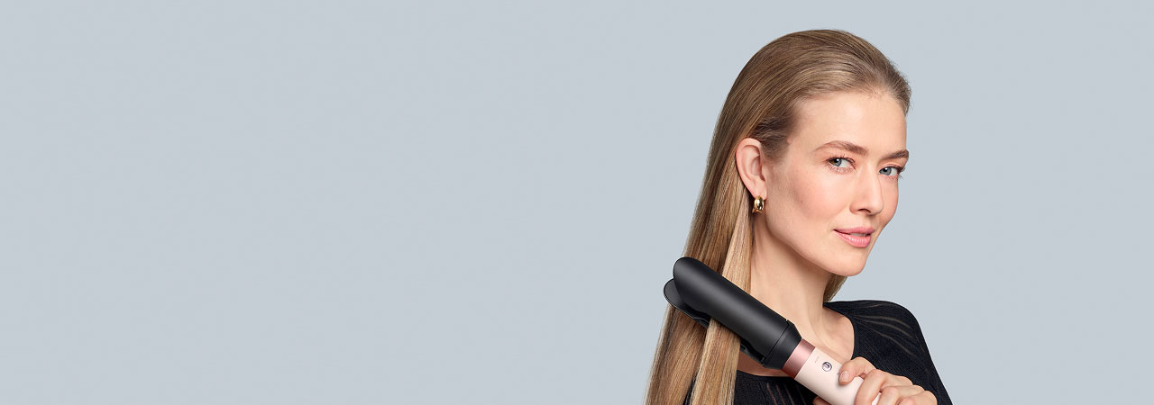Блондинка-модель розгладжує волосся за допомогою мультистайлера Dyson Airwrap Coanda2x.