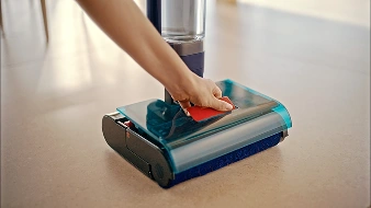 Рука відкриває кришку електричної щітки, щоб видалити накопичений бруд з лотка та бака