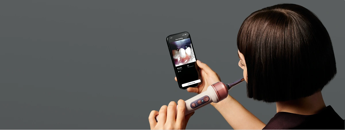 Модель чистить зуби зубною щіткою Dyson із вбудованою камерою, одночасно спостерігаючи за своїм ступенем чищення у застосунку.