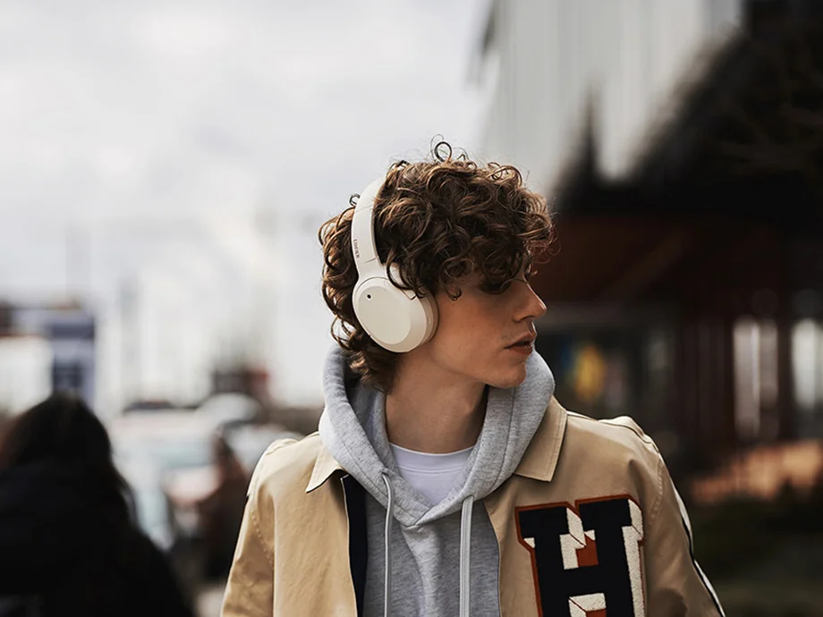 Чоловік у бежевих навушниках, який дивиться вбік, стоїть на тлі міської вулиці