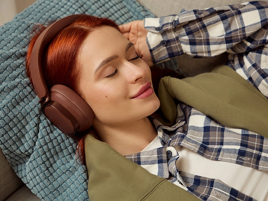 Рудоволоса дівчина в картатій сорочці відпочиває із заплющеними очима та в навушниках