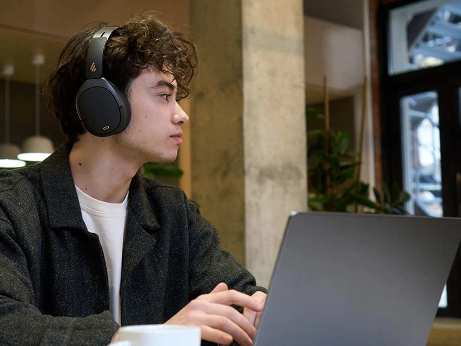 Молодий чоловік з кучерявим волоссям у темних навушниках-накладках дивиться вниз. На ньому сіра футболка.