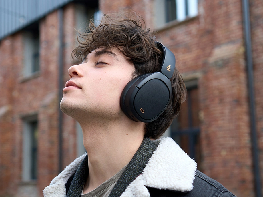 Людина з кучерявим волоссям у темних навушниках-накладках дивиться вгору і бачить джинсову куртку з хутряною обробкою.