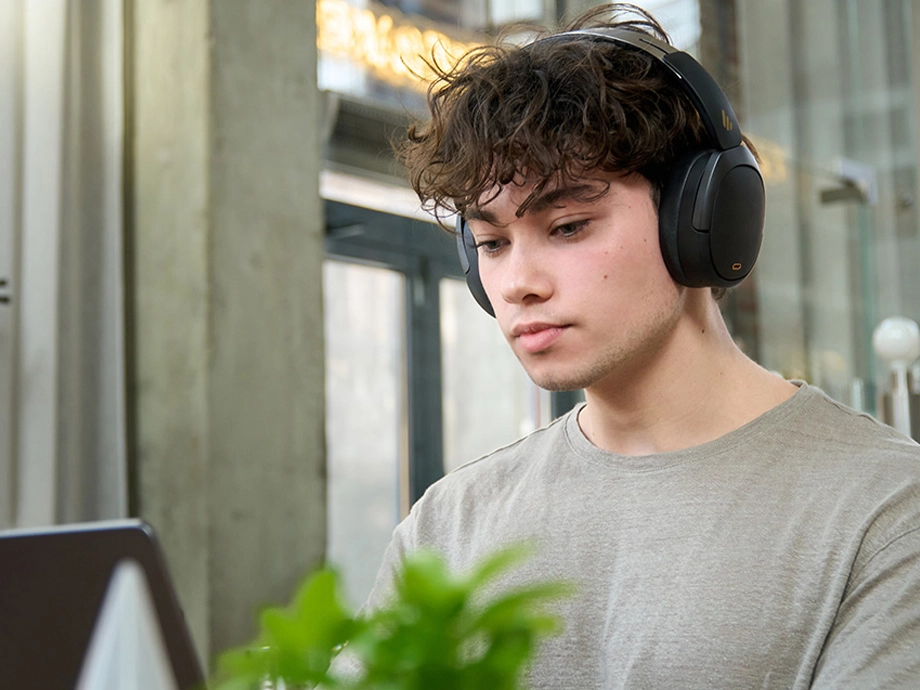 Кучерявий чоловік у темних навушниках-накладках дивиться вниз, перед ним стоїть квітка.