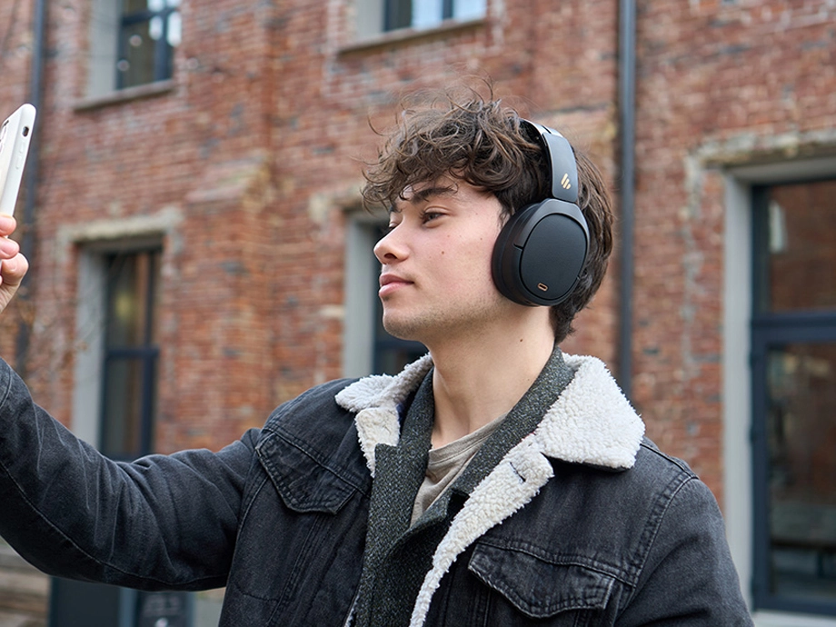 Чоловік з кучерявим волоссям у темних навушниках-накладках робить селфі