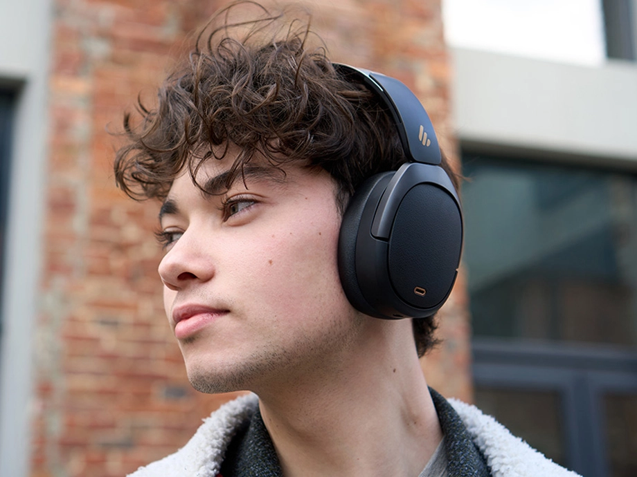 Чоловік з кучерявим волоссям у темних навушниках-накладках, зображений у профіль на вулиці.