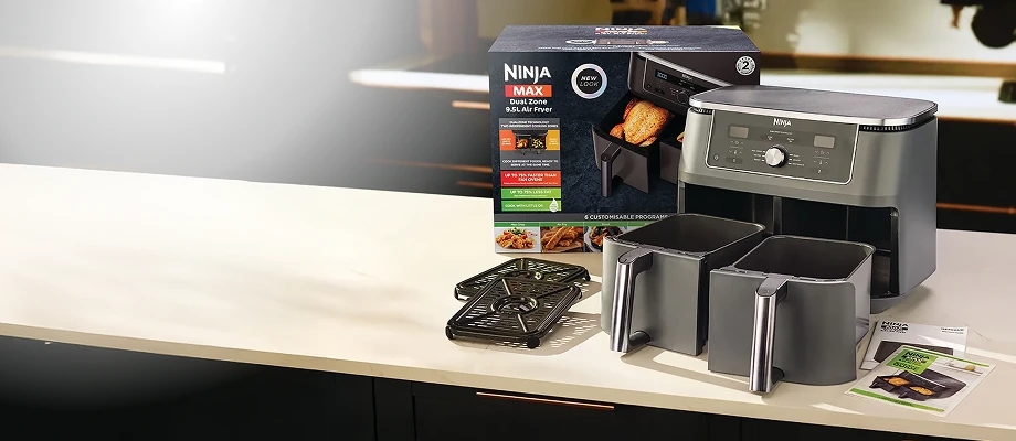 Аерофритюрниця Ninja, два кошики, решітка, інструкція з експлуатації та упаковка продукту стоять на яскравій кухонній стільниці.