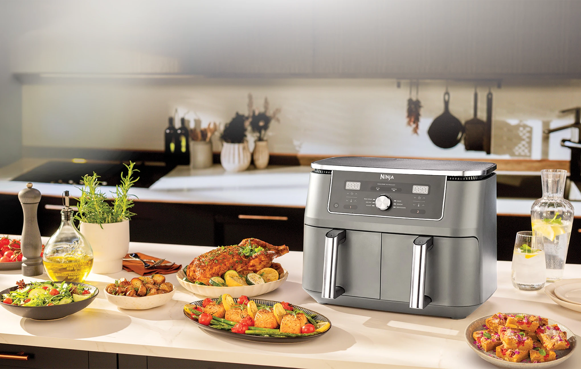 Срібна аерофритюрниця Ninja Foodi Max стоїть на кухонній стільниці, оточена різноманітними стравами для вечері.