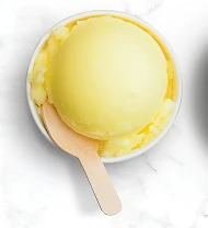 Жовтий заморожений йогурт у невеликій мисці з дерев'яною ложкою