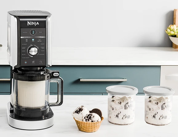 Морозивоварка Creami Deluxe на кухонному столі, порція морозива та два контейнери замороженого морозива на потім.