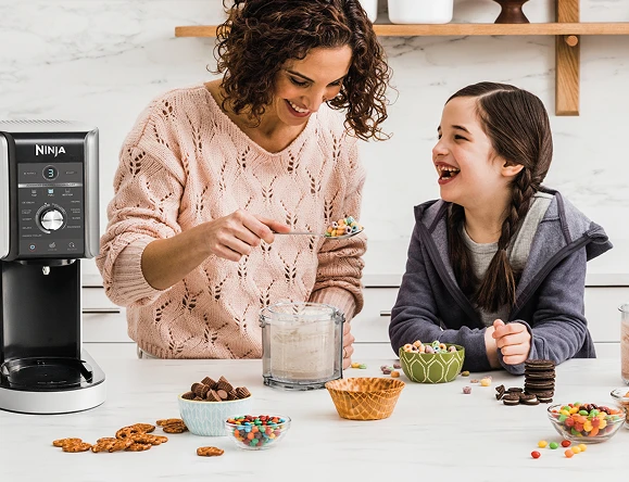 Мати та донька готують десерти на кухонному столі за допомогою морозивоварки Creami Deluxe.