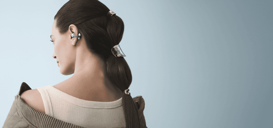 Голова та верхня частина спини довговолосої жінки, що стоїть задом наперед із синім навушником FreeClip 2 у вусі