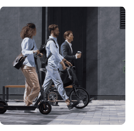 Люди на вулиці. Чоловік з кавою та інший з велосипедом у навушниках FreeClip 2, а жінка зі самокатом дивиться на них.