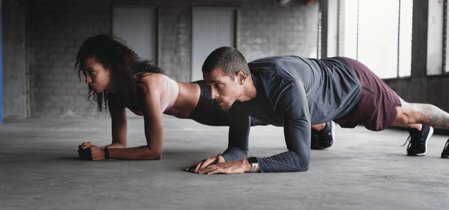 Жінка та чоловік у спортивному одязі виконують планку на бетонному майданчику. Чоловік у навушниках FreeClip 2.