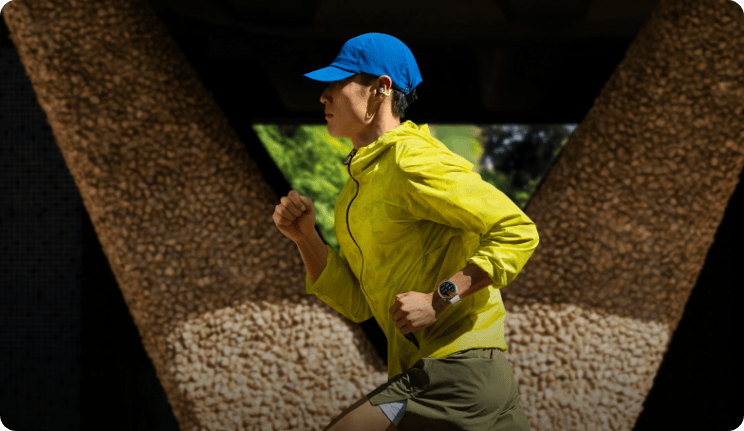 Чоловік у яскравому спортивному одязі та кепці біжить на тлі будівлі, на ньому годинник HUAWEI Watch GT Runner 2.