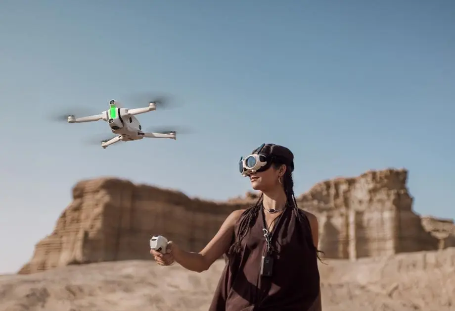 Жінка на дюні в окулярах Vision керує дроном за допомогою контролера руху Grip.