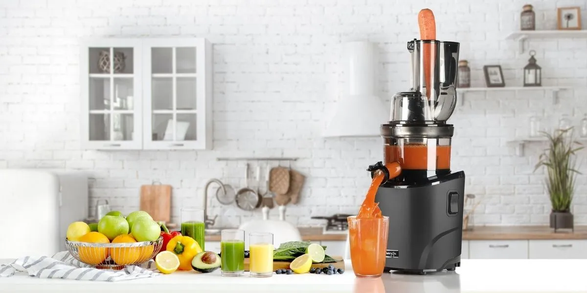 Соковижималка Black Kuvings Revo830 з морквою в контейнері та апельсиновим соком у склянці