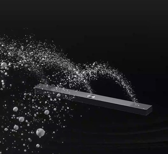LG Soundbar na czarnym tle odsłania swój design, zaczynając od góry i przechodząc do rogu. Białe krople wydobywają się z centralnej i końcowej części soundbara niczym wodospad, obrazując wystrzałowy dźwięk.