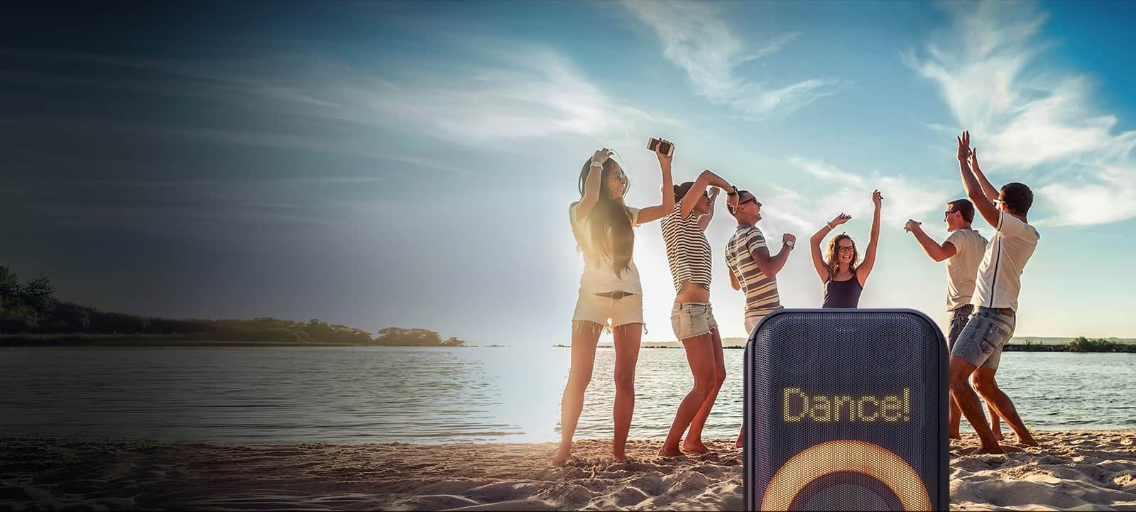 Zbliżenie na dynamiczne oświetlenie pikselowe. Wyświetla taniec! Tekst. Poniżej na pomarańczowo świeci się wielokolorowe oświetlenie pierścienia. Za głośnikiem, ludzie tańczą na plaży.