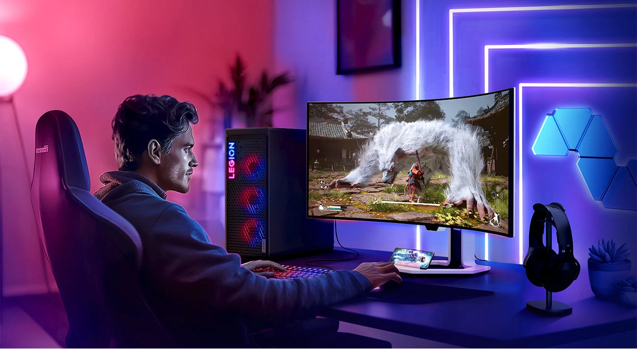 Монітор Lenovo Legion Pro 34WD-10 на столі, перед яким сидить молода людина та грає в комп'ютерну гру