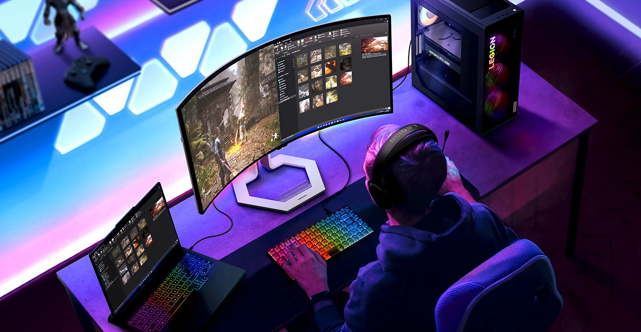 На столі видно монітор Lenovo Legion Pro 34WD-10, відкритий ноутбук і робоча станція, а також клавіатуру з підсвічуванням.