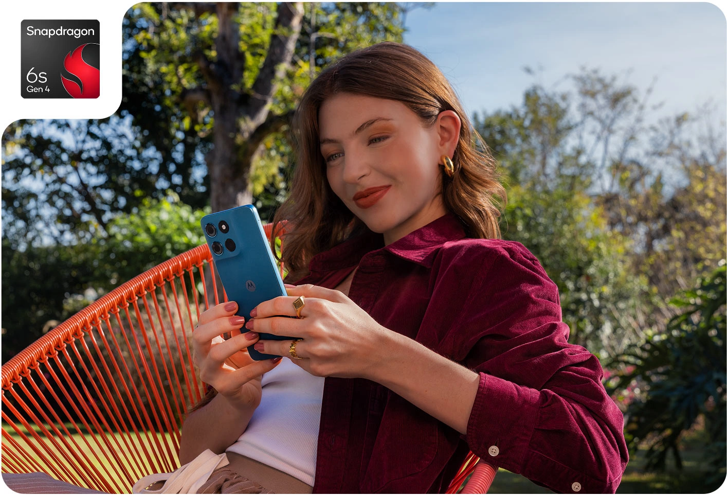 Дівчина в бордовій сорочці сидить у садовому кріслі та користується смартфоном Moto G57 Power.