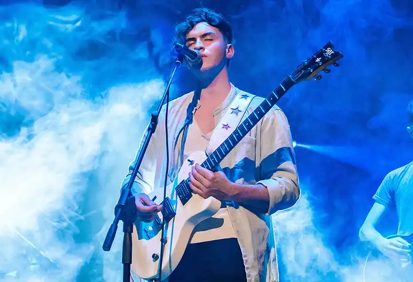 Muzyk grający na gitarze i śpiewający na scenie w&nbsp;otoczeniu dymu.