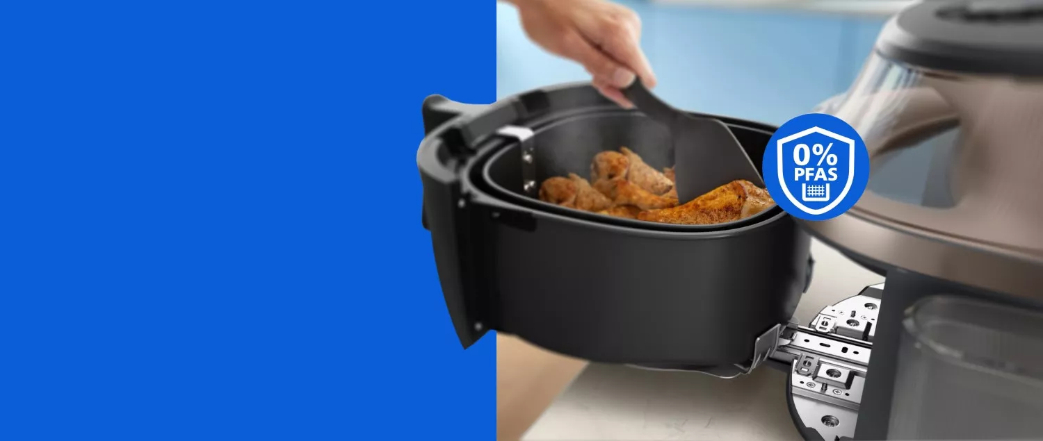 Жінка використовує лопатку, щоб перевертати курячі гомілки в кошику аерофритюрниці.