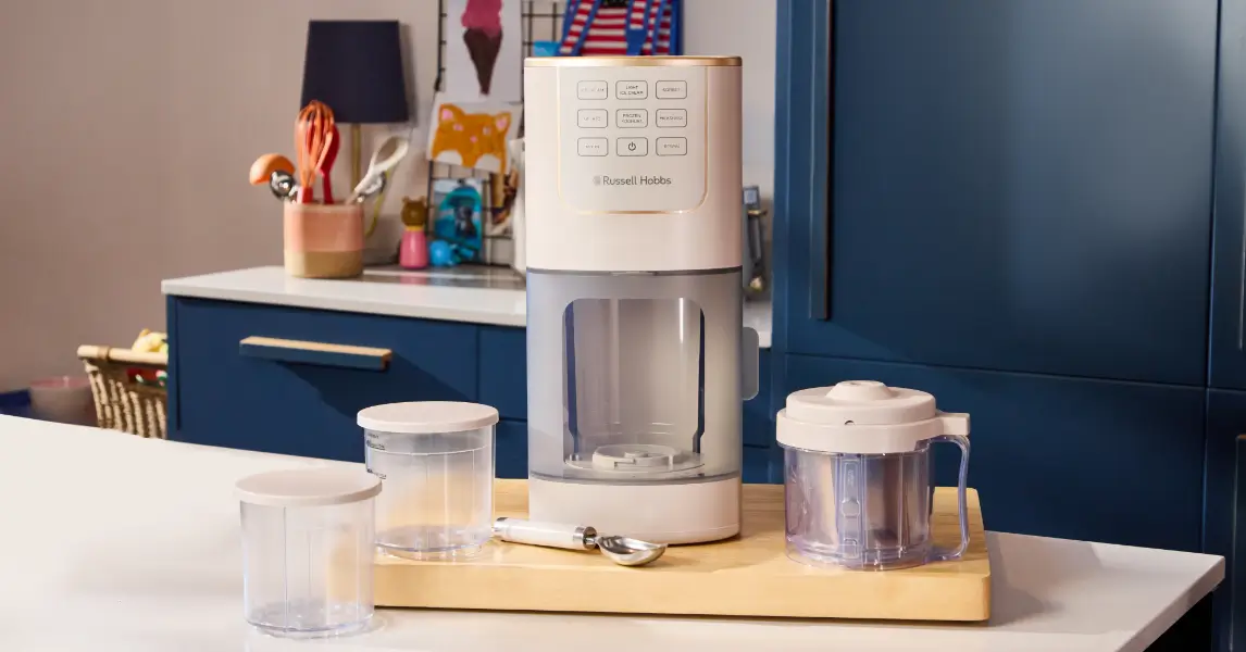 Морозивоварка Russell Hobbs Chilluxe на дерев'яній дошці з 3 контейнерами поруч з машиною та ложкою для морозива