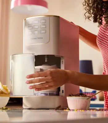 Жінка вставляє основу в морозивоварку Russell Hobbs на стільниці; на задньому плані — рожево-біла миска.