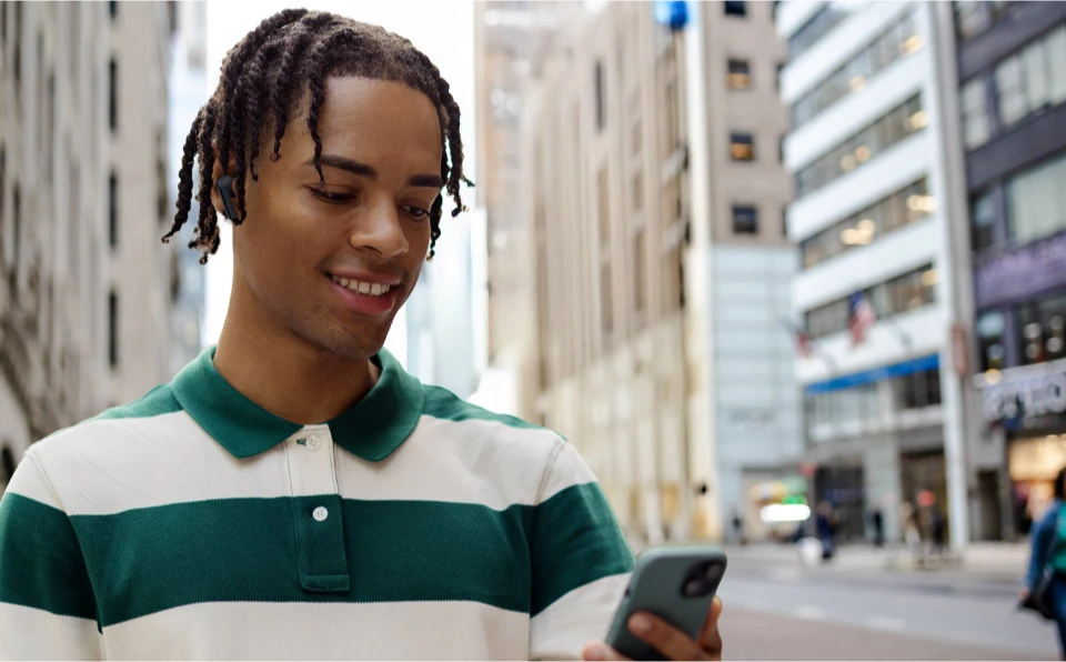 Чоловік у чорних навушниках Galaxy Buds3 FE надворі, на тлі міського пейзажу.