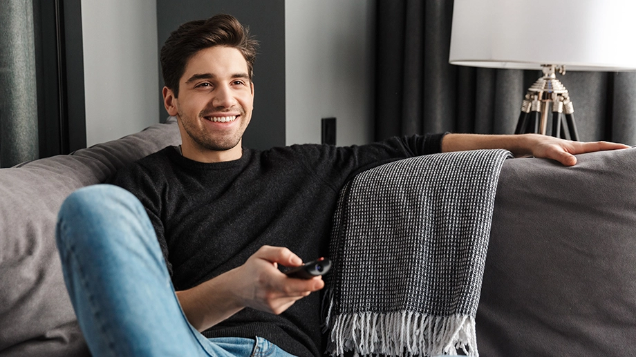 Щасливий чоловік сидить на дивані з пультом дистанційного керування телевізором