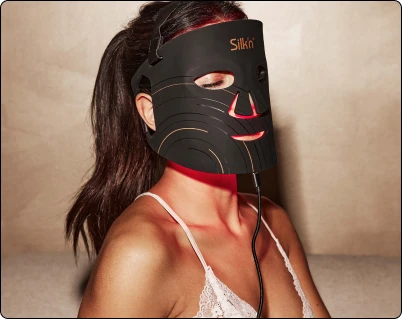 Жінка в білизні носить чорну маску Silk'n LED (світлодіодна) на обличчі, яка випромінює червоне світло.