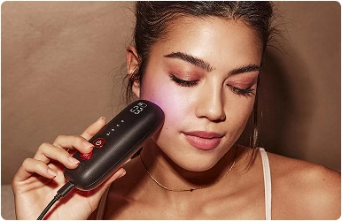 Жінка використовує чорний портативний пристрій світлотерапії Silk'n LED (світлодіод) на щоці.